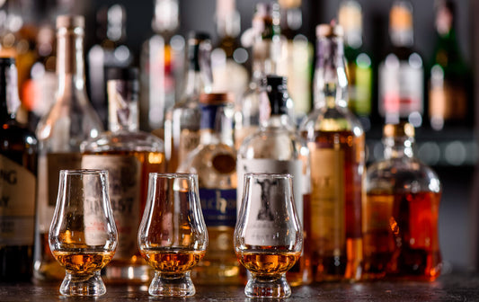 Three Glencairn Glass with whiskey on a bar wooden counter close up on the background of blurry bottles. Close up. Dark background