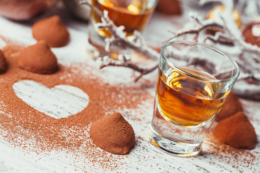 glass of whiskey next to chocolate truffles with a heart-shaped pattern