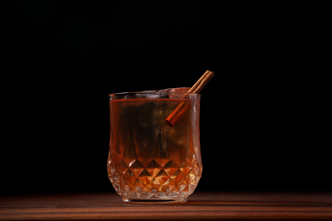 Cinnamon Old Fashioned cocktail on a walnut bar table